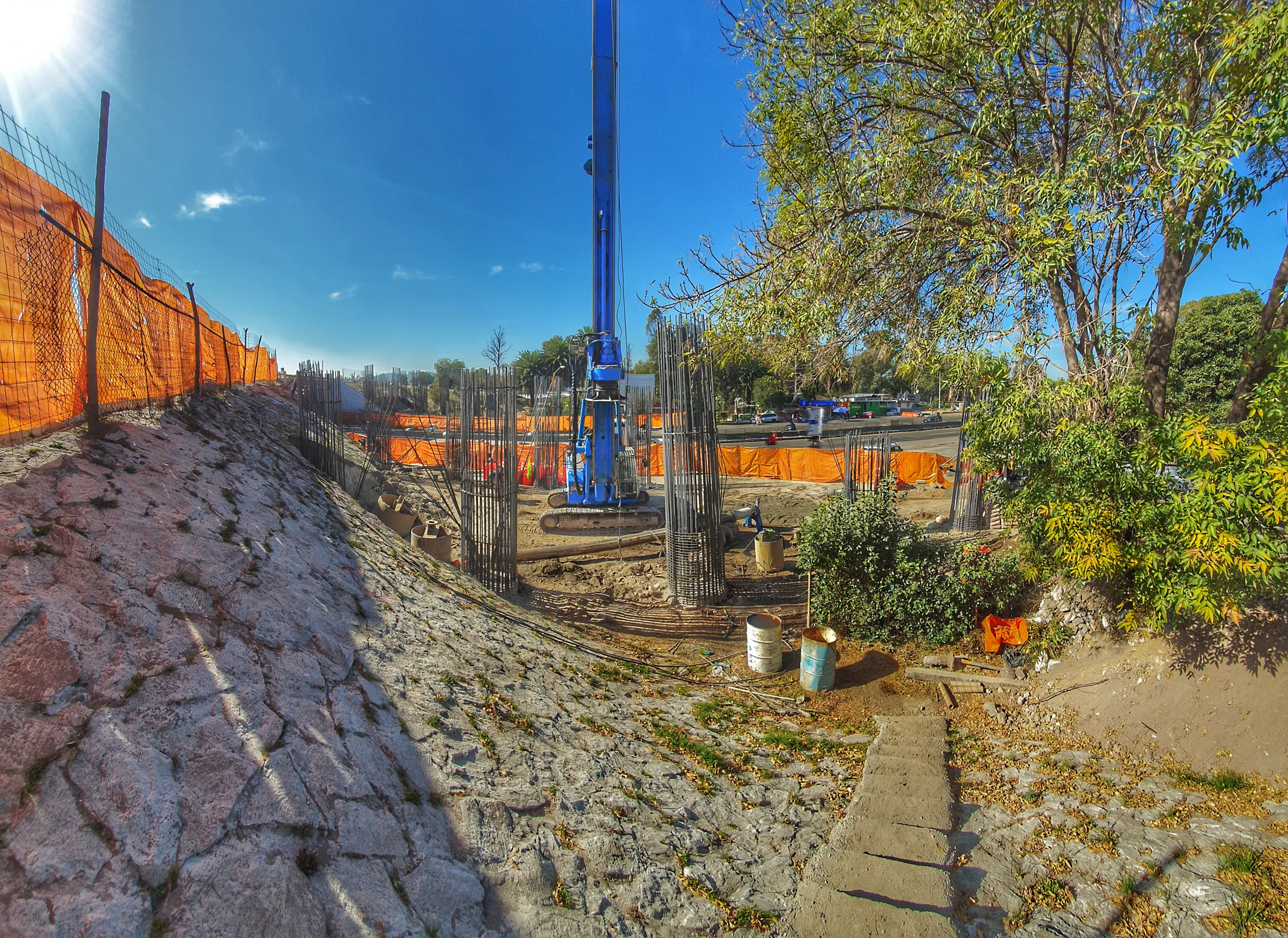 Equipo de perforación azul y personal trabajando detrás de una malla de seguridad en un terreno abierto.